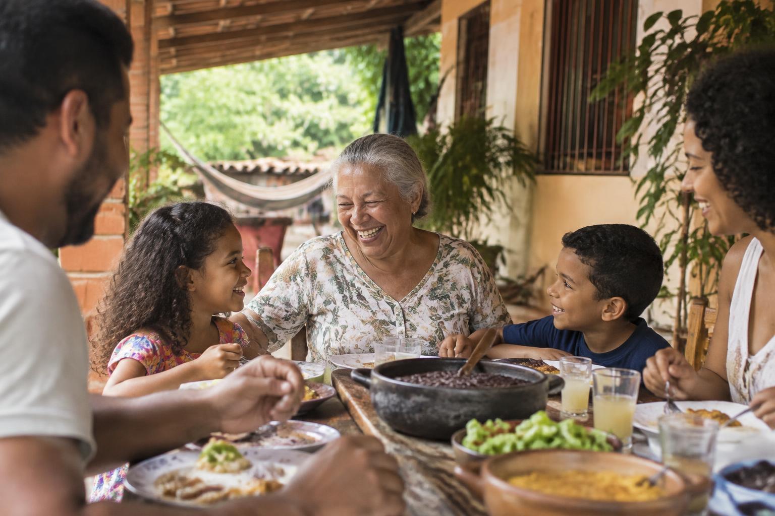 Família brasileira de várias gerações reunida em um almoço de domingo na varanda